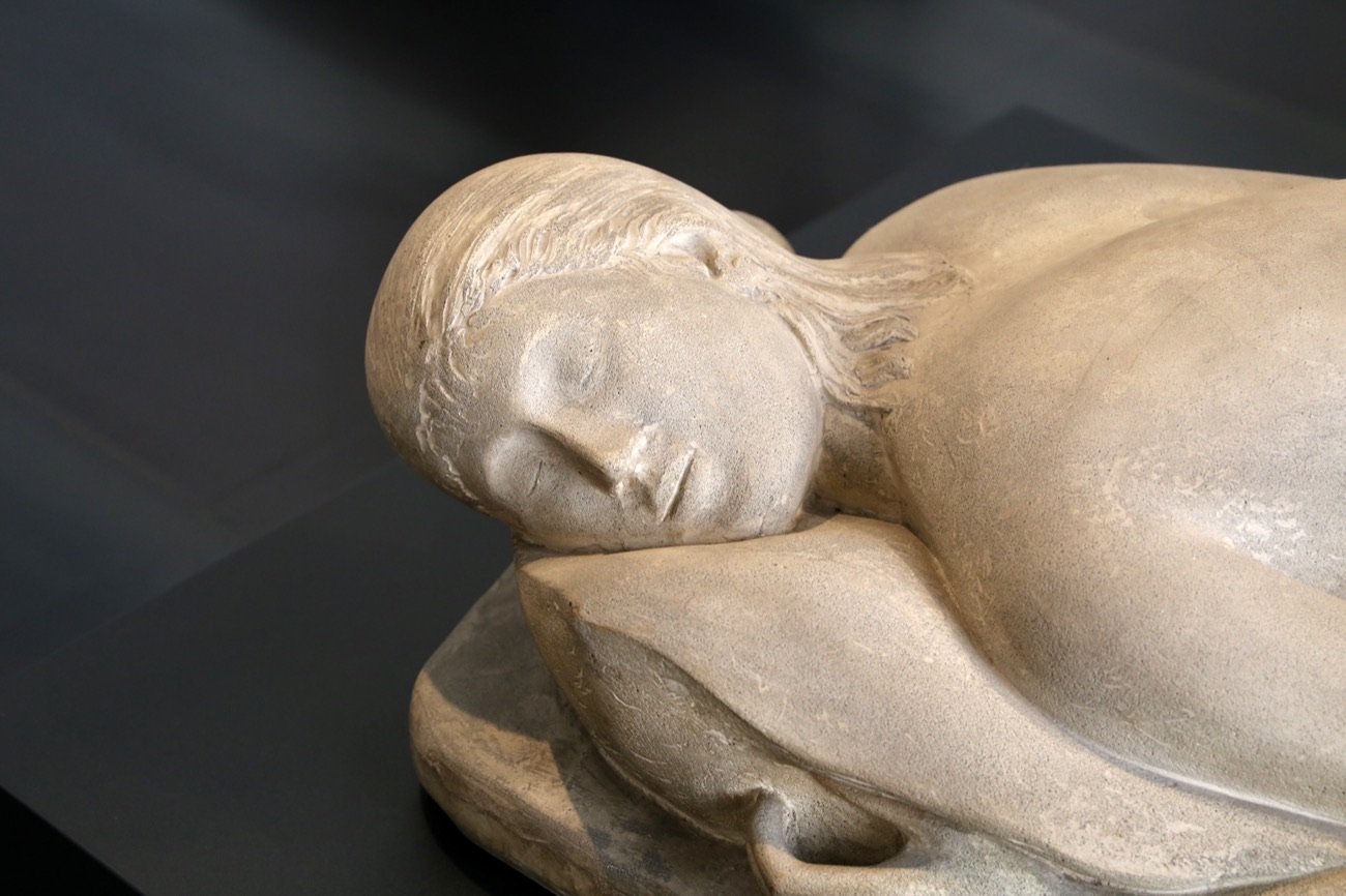 «La Pisana» di Arturo Martini, scultura in pietra di una giovane donna distesa, con la testa reclinata e gli occhi chiusi